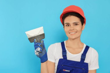 Professional worker in hard hat with putty knife on light blue background