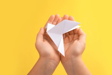 Origami art. Child holding paper bird on yellow background, closeup