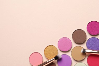 Different beautiful eye shadows and makeup brushes on beige background, flat lay. Space for text