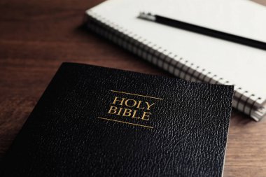 Holy Bible and notebook with pencil on wooden table, closeup. Religious book