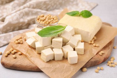 Delicious tofu cheese, basil and soybeans on light gray table, closeup