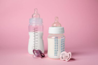 Feeding bottles with milk and baby pacifiers on pink background