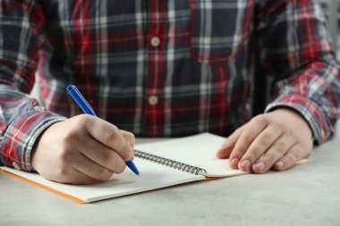 Man writing with pen in notebook at white table, closeup