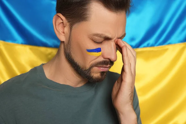 Sad man with face paint near Ukrainian flag, closeup