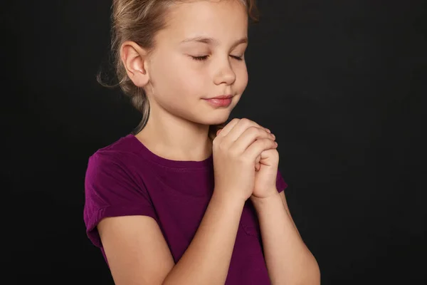Girl with clasped hands praying on black background, closeup