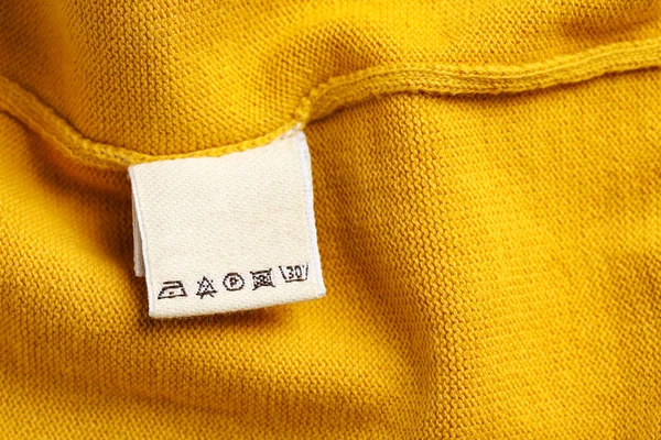 Clothing label on beautiful yellow garment, top view. Space for text