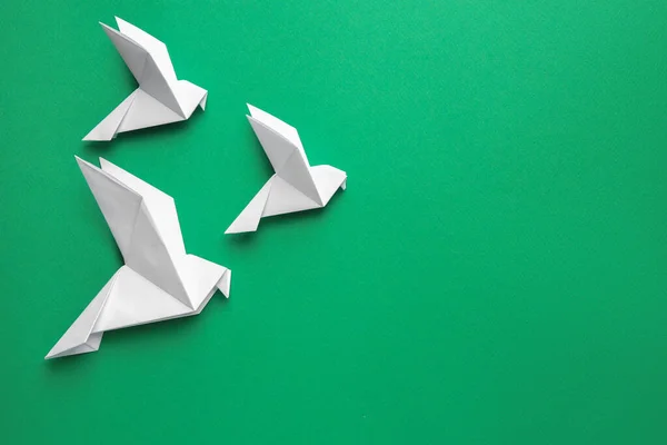 Beautiful white origami birds on green background, flat lay. Space for text