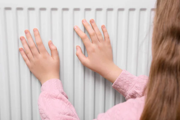 Girl warming hands on heating radiator, closeup