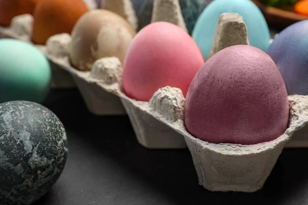 Easter eggs painted with natural organic dyes on black table, closeup. Space for text