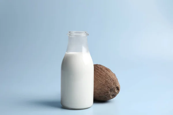 Glass bottle of delicious vegan milk and coconut on light blue background