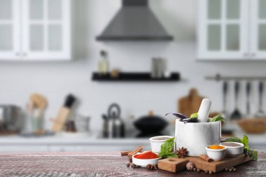 Mortar and different spices on wooden table in kitchen. Space for text