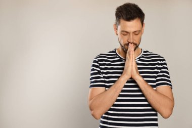 Ellerini sıkıca bağlayıp açık gri arka planda dua eden adam. Metin için boşluk