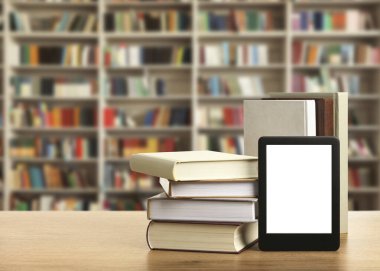 Hardcover books and modern e-book on wooden table in library. Space for text