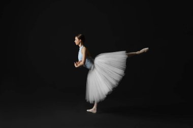 Young ballerina practicing dance moves on black background