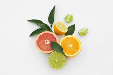 Different citrus fruits and leaves on white background, top view
