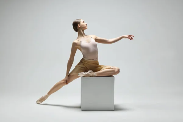 Young ballerina practicing dance moves on cube against white background