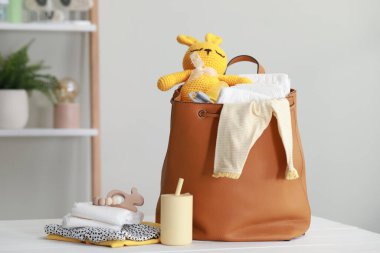 Mother's bag with baby's stuff on white wooden table indoors
