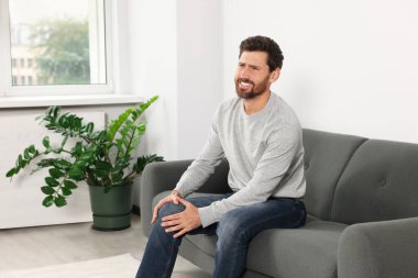 Man suffering from leg pain on sofa in room