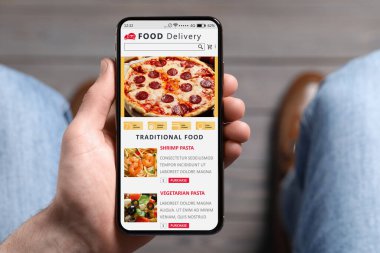 Food delivery service. Man choosing dish from menu on site using smartphone indoors, closeup