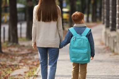 Young mom taking her son to school, back view