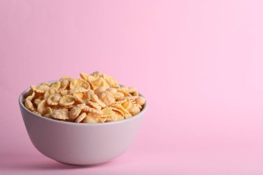 Bowl of tasty crispy corn flakes on pale pink background, space for text
