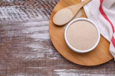 Bowl and spoon with active dry yeast on wooden table, top view. Space for text