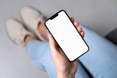 Woman holding smartphone with blank screen indoors, top view. Mockup for design