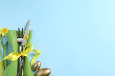 Cutlery set, Easter eggs and narcissuses on light blue background, flat lay with space for text. Festive table setting