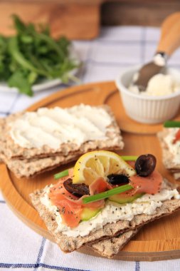 Fresh crunchy crispbreads with cream cheese, salmon, olives, lemon and green onion on table, closeup