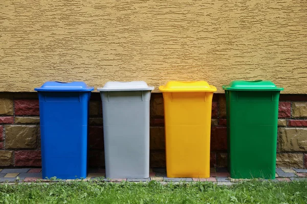 Many colorful recycling bins near yellow wall outdoors