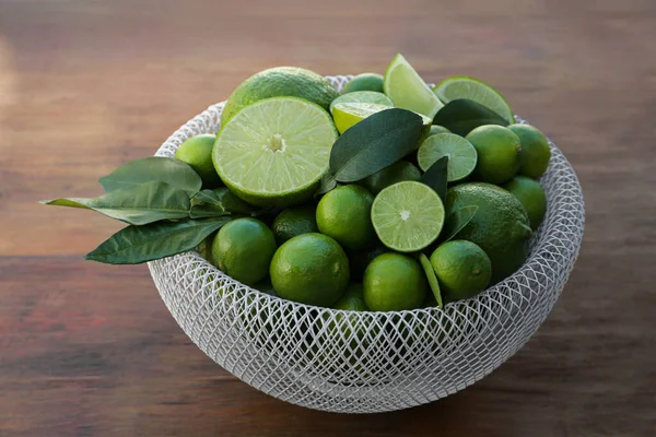Fresh ripe limes and green leaves in bowl on wooden table