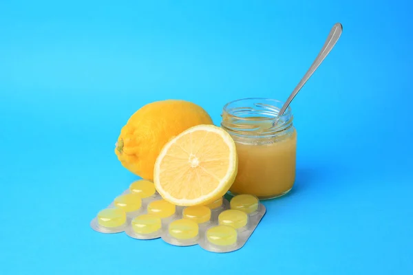 Blister with cough drops, fresh lemons and honey on light blue background
