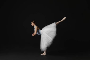 Young ballerina practicing dance moves on black background. Space for text