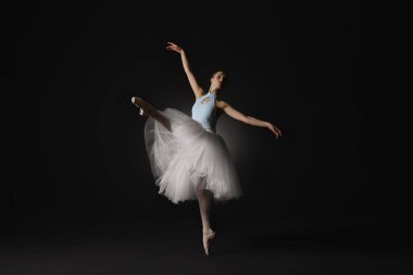 Young ballerina practicing dance moves on black background