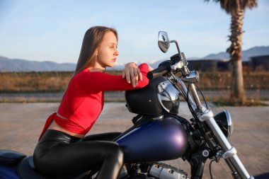 Beautiful young woman with helmet sitting on motorcycle outdoors