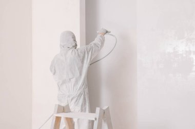 Üniformalı dekoratör. Duvarı spreyle boyuyor. Kapalı, arka manzaralı.