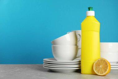 Clean tableware, dish detergent and lemon on grey table against light blue background. Space for text