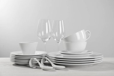 Set of clean dishware and glasses on white wooden table against light background