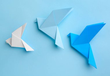 Origami art. Colorful handmade paper birds on light blue background, flat lay