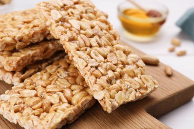 Board with tasty kozinaki bars, peanuts and honey on table, closeup