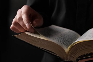 Woman reading holy Bible on black background, closeup