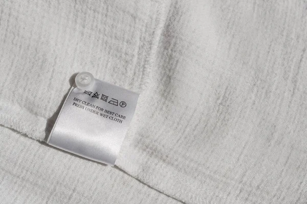 Clothing label with instruction on white garment, top view. Space for text