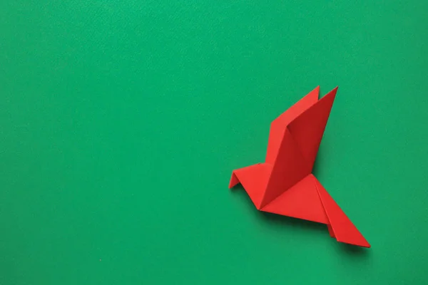 Beautiful red origami bird on green background, top view. Space for text