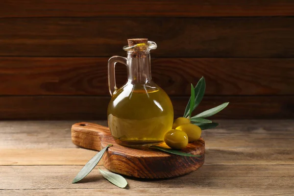 Jug of cooking oil, olives and green leaves on wooden table