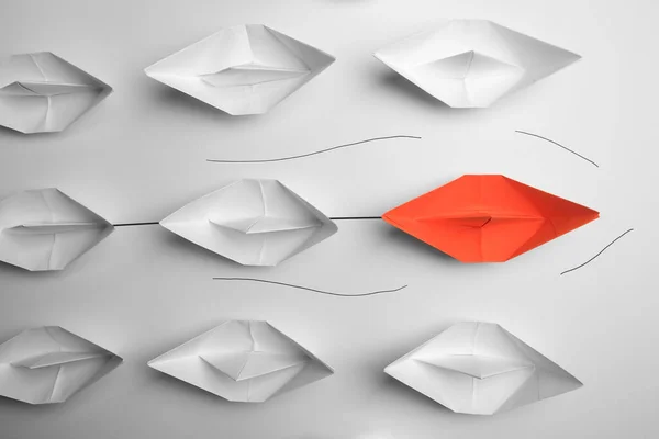 Group of paper boats following orange one on white background, flat lay. Leadership concept