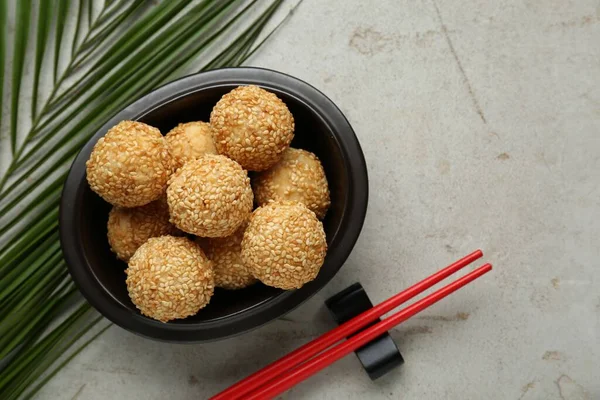 Delicious sesame balls, green leaf and chopsticks on textured table, flat lay. Space for text