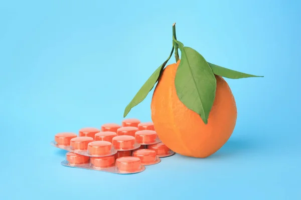 Fresh orange and blisters with cough drops on light blue background