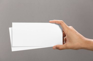 Man holding flyers on grey background, closeup. Mockup for design