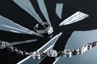 Luxury jewelry. Stylish presentation of elegant ring and bracelet on black mirror surface with broken glass, closeup