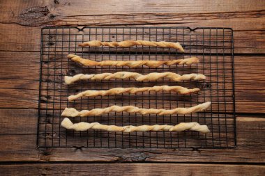 Rack with homemade breadsticks on wooden table, top view. Cooking traditional grissini